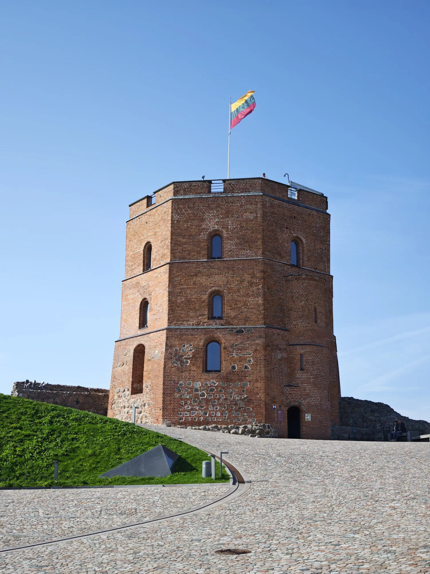 Gediminas' Tower, the red-brick remains of the upper castle on its hill above Vilnius, a Lithuanian flag on top.