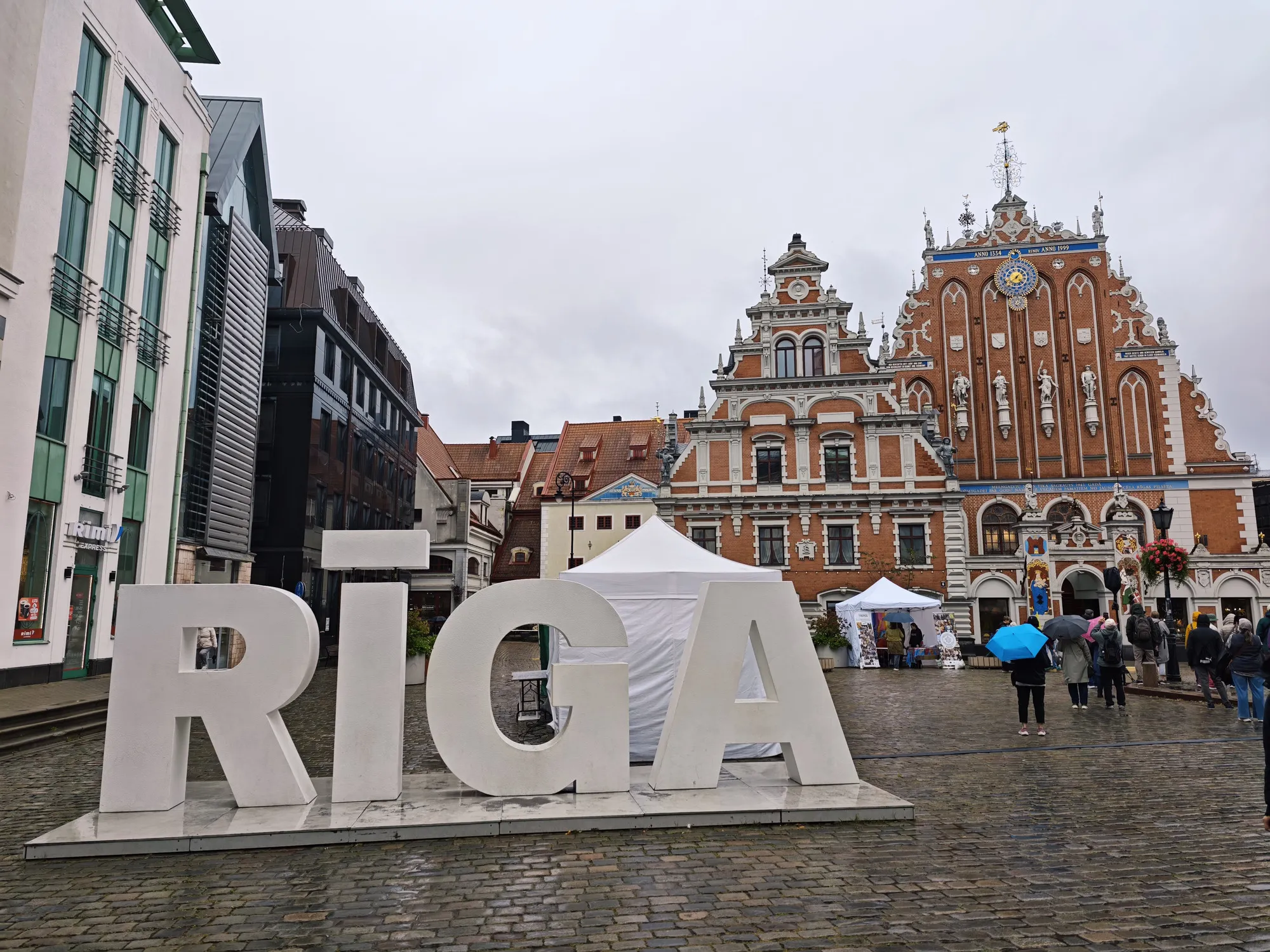 Riga's town hall square on a grey, wet morning: the big RĪGA letters in front of the gabled House of the Blackheads.