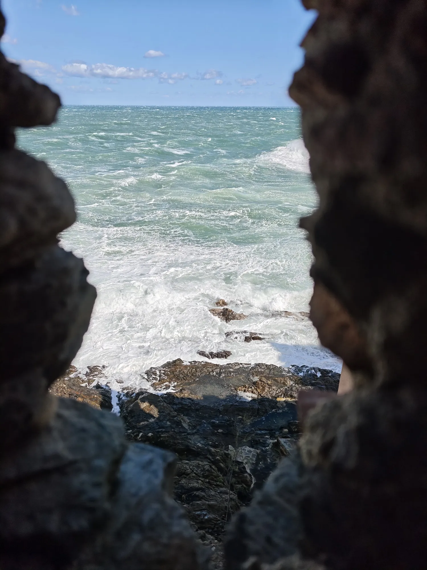 The Mediterranean breaking white on the rocks at Collioure, seen through a gap in the stone.