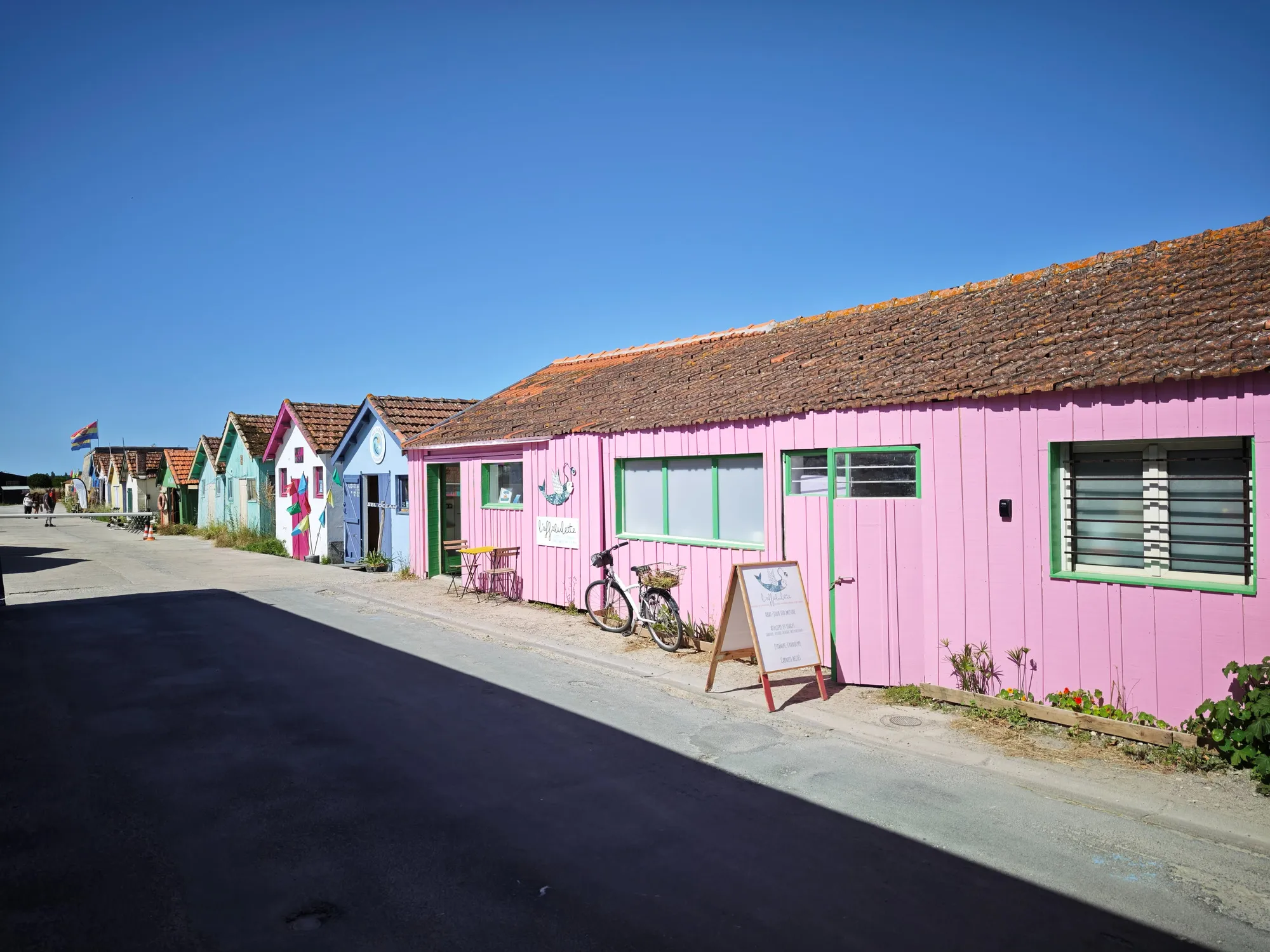 The repainted oyster cabins at the harbour of Le Château-d'Oléron, lined up in faded pink and blue under a hard blue sky.